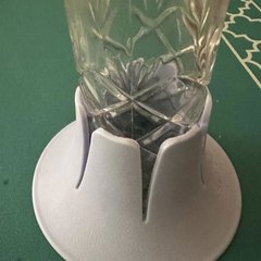 A pale blue-grey drink base holding a cut-crystal tumbler of water on a green felt table with a white trellis-pattern border